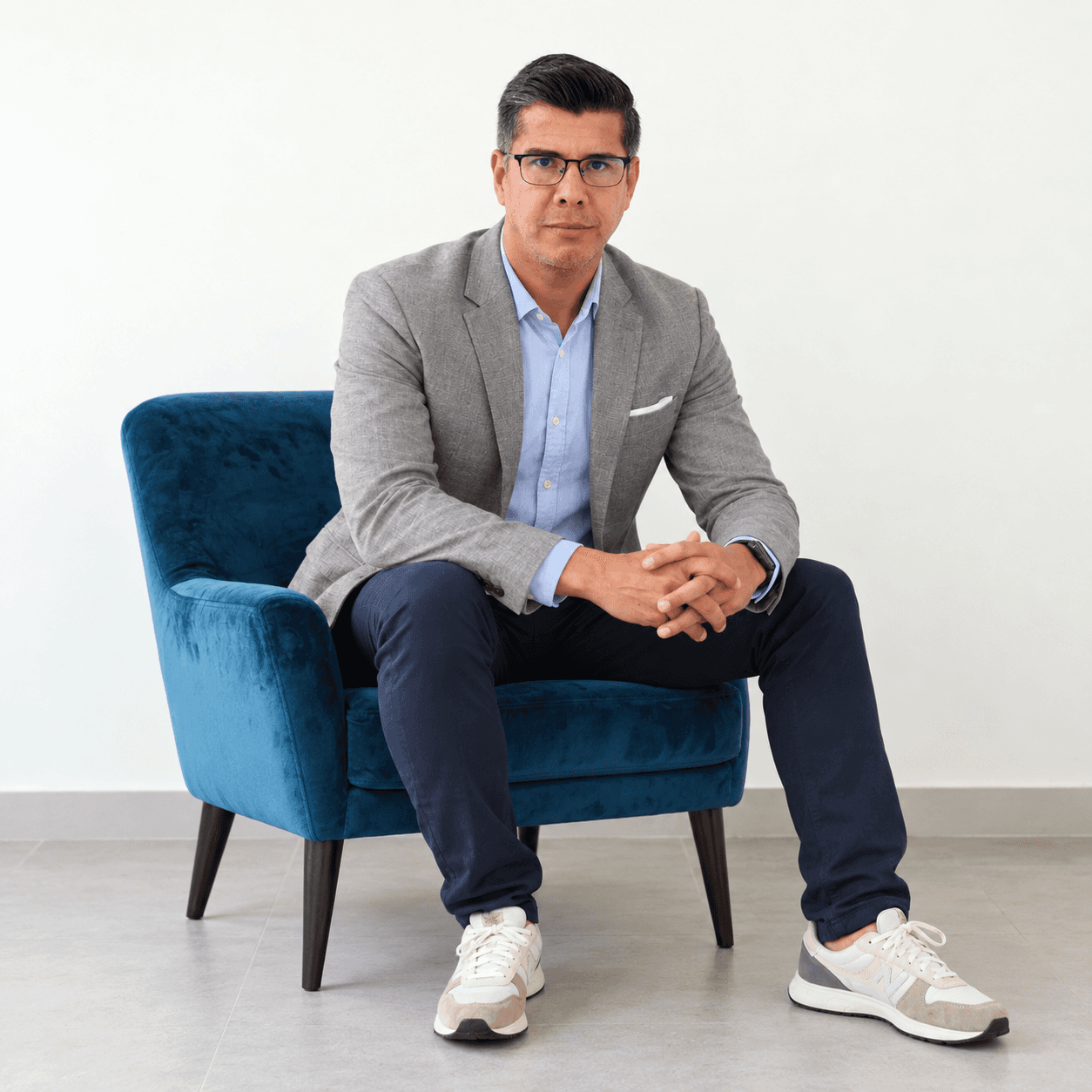 Ronald Thamez sentado en sillón teal, composición de cuerpo completo